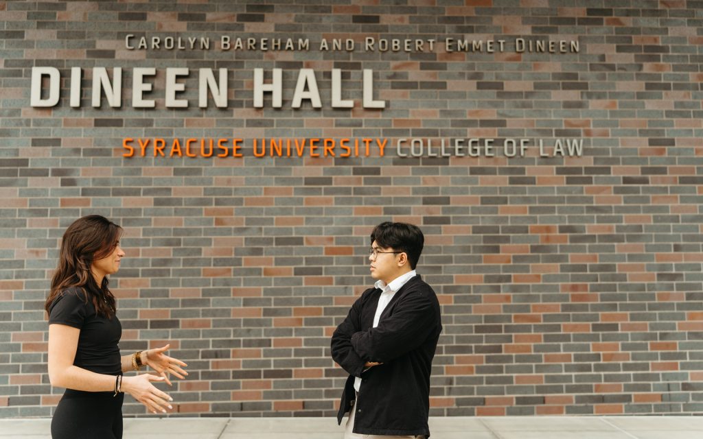 Peterson and Ortizo chat together in front of the brick facade of Dineen Hall