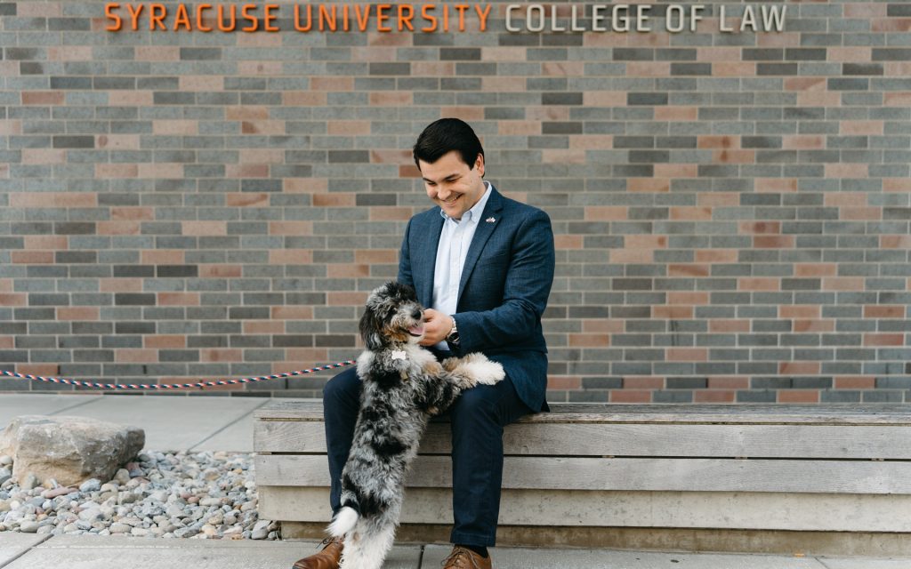 A man in a suit pets a dog in front of a brick wall