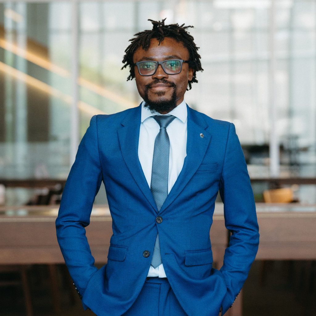 Sinésio Sambo stands in the library smiling in a blue suit and a white shirt