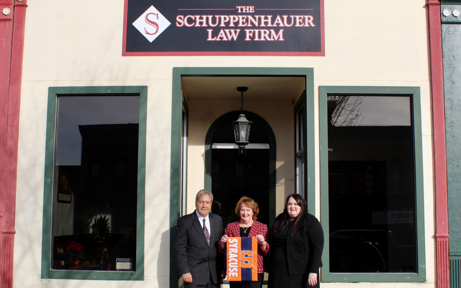 The Schuppenhauers in front of their law firm holding a Syracuse University banner