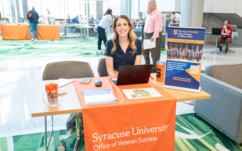 able covered with an orange cloth. Brochures and promotional materials are displayed on the table.