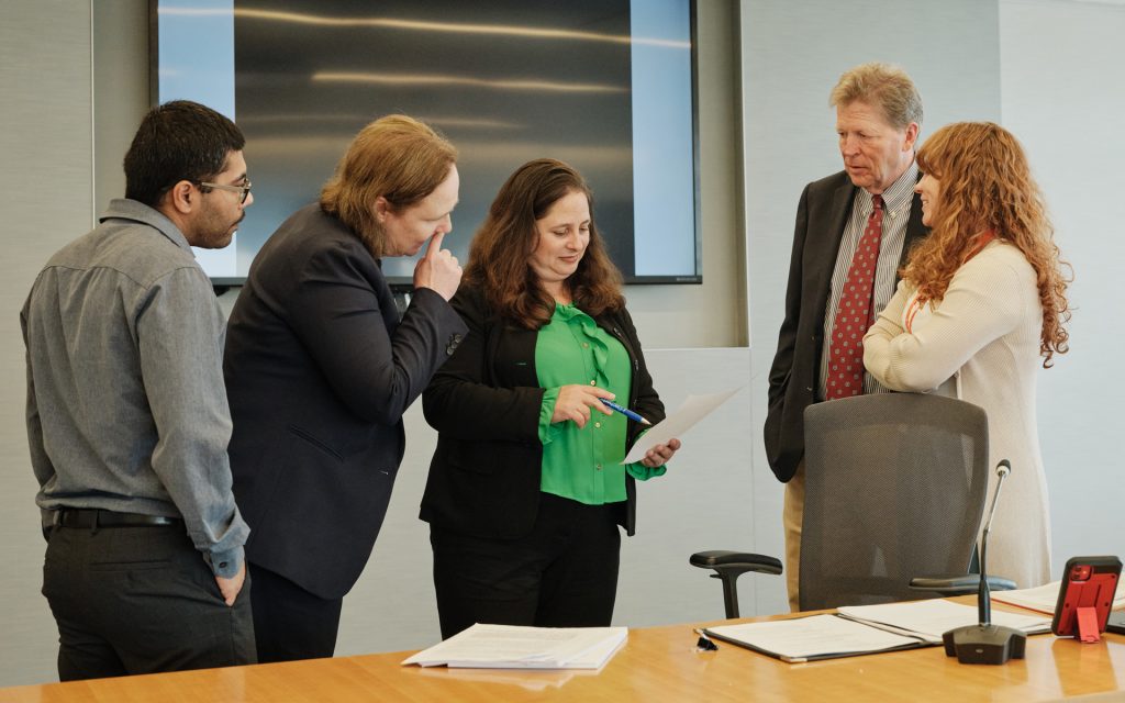 Students gather around a professor who explains concepts while pointing at a document