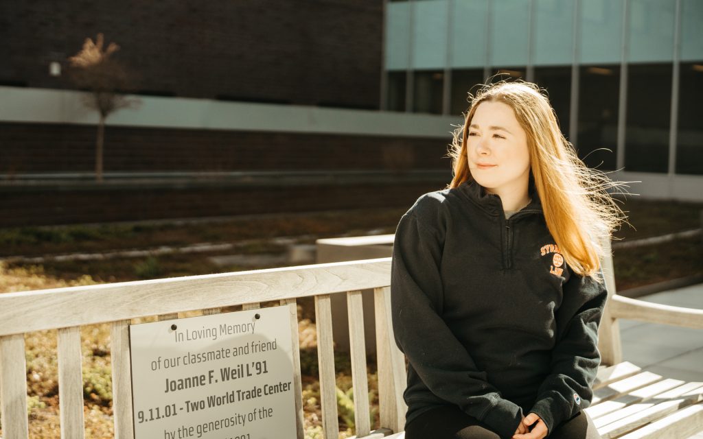 Meghan Wright sits outside on a bench in memory of an alum who passed away in the attack on the World Trade Center in 2001