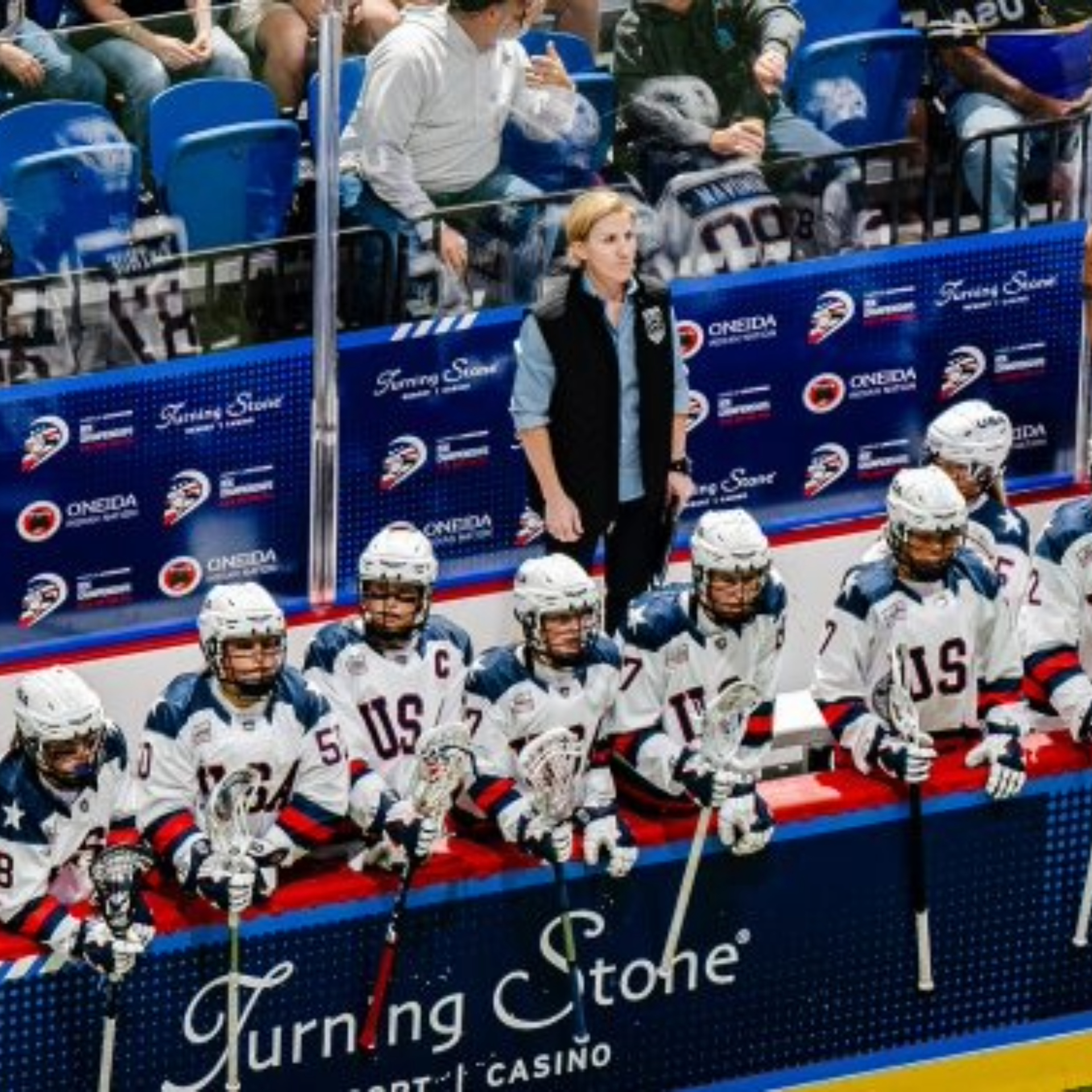 Ginny Capicchioni standing on the bench behind her USA lacrosse team, coaching