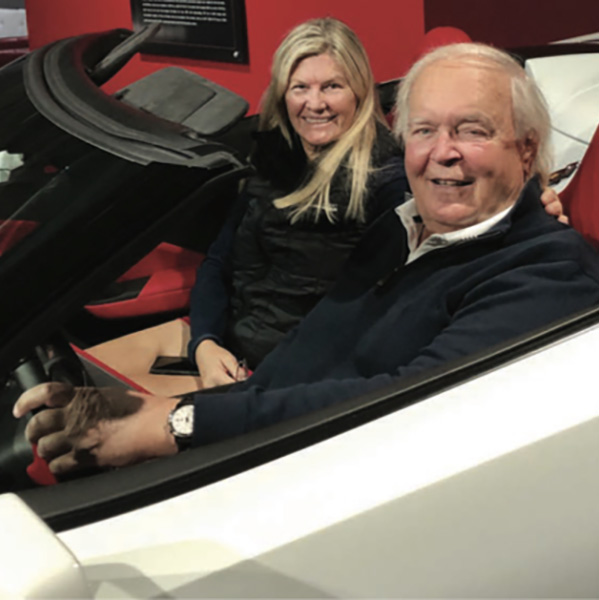 man and woman witting in a white convertible car, smiling at the camera