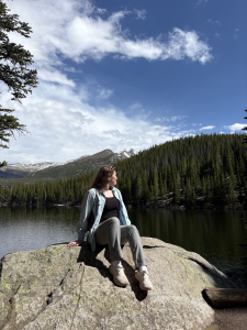 Meghan Snelling at Rocky Mountain National park sitting on a rock with water behind her. 