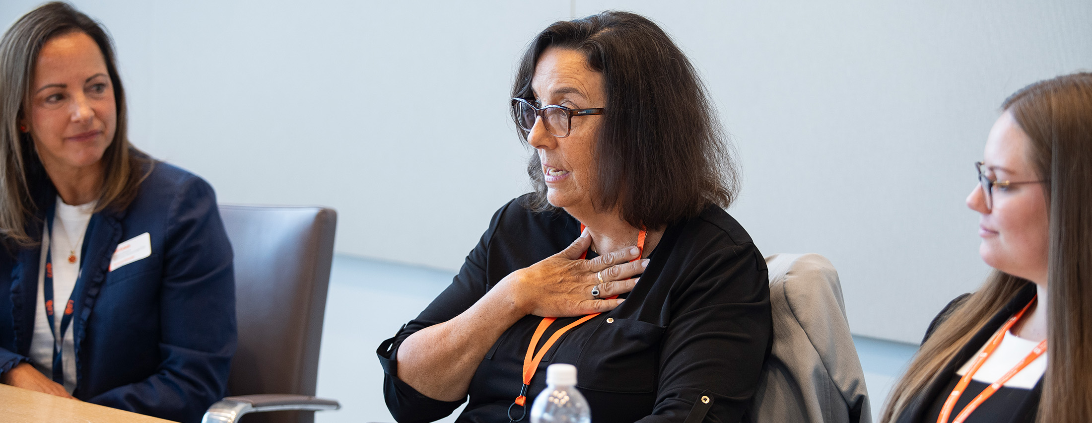 Judge Dancks speaking on a panel with two other women, talking with glasses on and her hand on her chest in a gesture while speaking