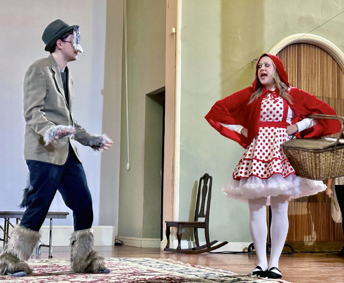 A man dressed in a wolf costume approaches a woman dressed as little Red Riding Hood on stage